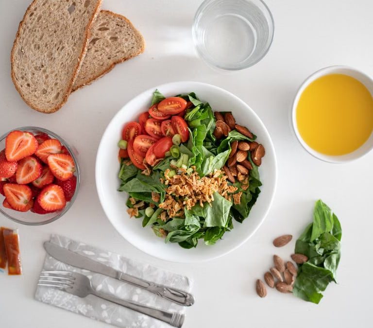 Top view of a healthy salad and fresh ingredients with bread and juice on a white surface.